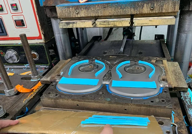 Open steel mold on a workbench with molded silicone parts being inspected by hand during trial sampling